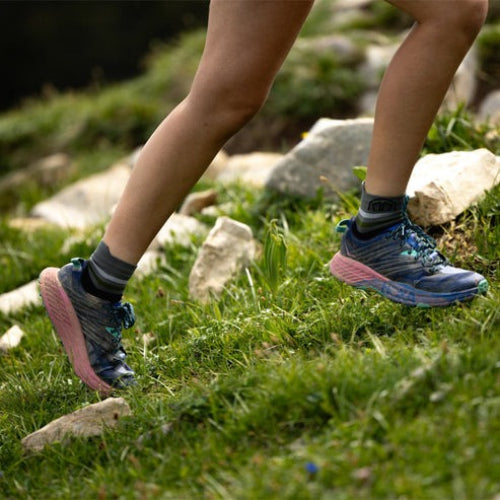 Person wearing Sidas running black ankle socks and blue running shoes on a grassy trail