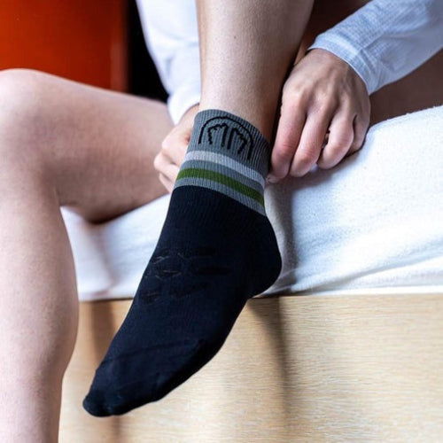 Person wearing Sidas ankle running socks in black with a pattern, sitting on a wooden floor.