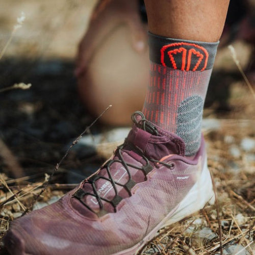 Person wearing a Sidas trail sock with a logo and a hiking shoe in a natural setting