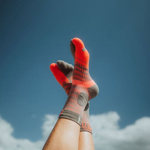 Orange and gray patterned Sidas trail socks against a blue sky with clouds
