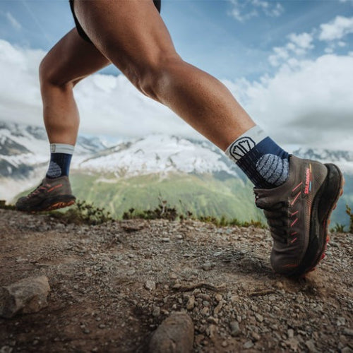 Person hiking on a mountain trail wearing outdoor shoes and socks.